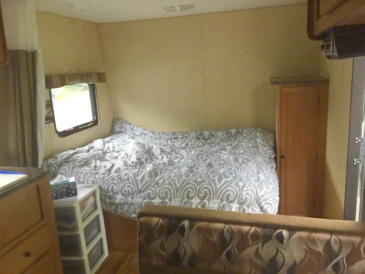 Inside this RV rental: a cozy bedroom with a patterned comforter, window, cabinet, and living area seating.. Bobcat Bobcat Trailer 2013