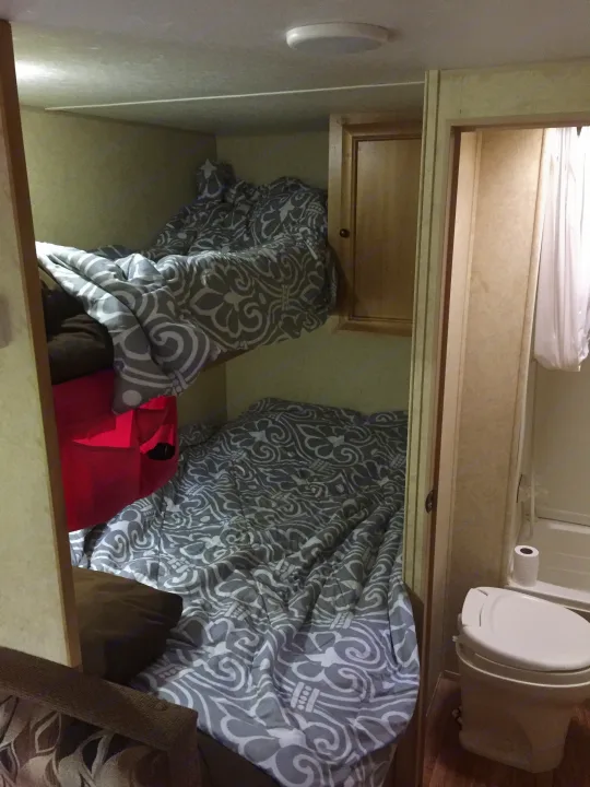 An RV rental's interior with two beds featuring patterned comforters, a cabinet, and a compact bathroom.. Bobcat Bobcat Trailer 2013