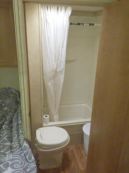 Inside a compact RV rental, showing the bathroom area with a shower, toilet, and patterned bedding.. Bobcat Bobcat Trailer 2013