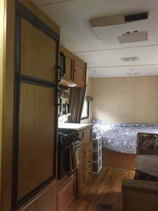 Looking down into an RV rental interior: kitchen with stove and wood cabinetry, alongside a patterned curtain for the living/sleeping area.. Bobcat Bobcat Trailer 2013
