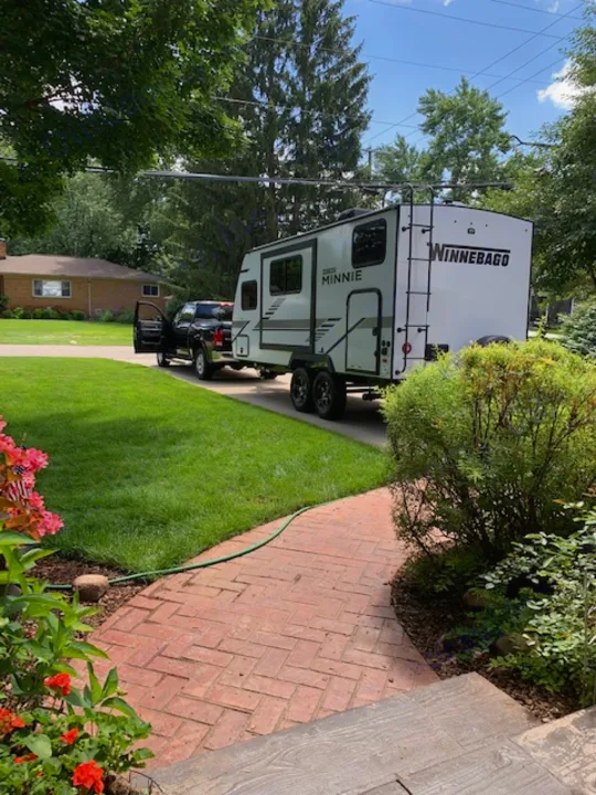 White Winnebago Minnie RV rental on driveway with pickup truck, next to a green lawn and brick path.. Winnebago Micro Minnie 2021
