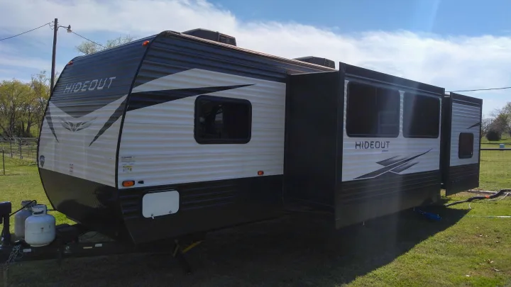 A large white and black Hideout travel trailer, perfect for an RV rental, is parked with slide-outs extended on green grass.. Keystone Hideout 2021