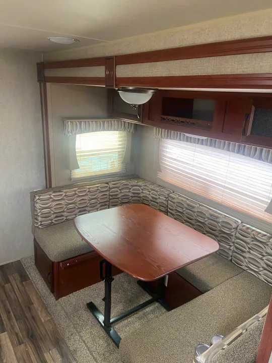 Cozy RV rental dinette area featuring U-shaped bench seating with patterned cushions, a wooden table, and windows with blinds.. Palomino Puma 2015