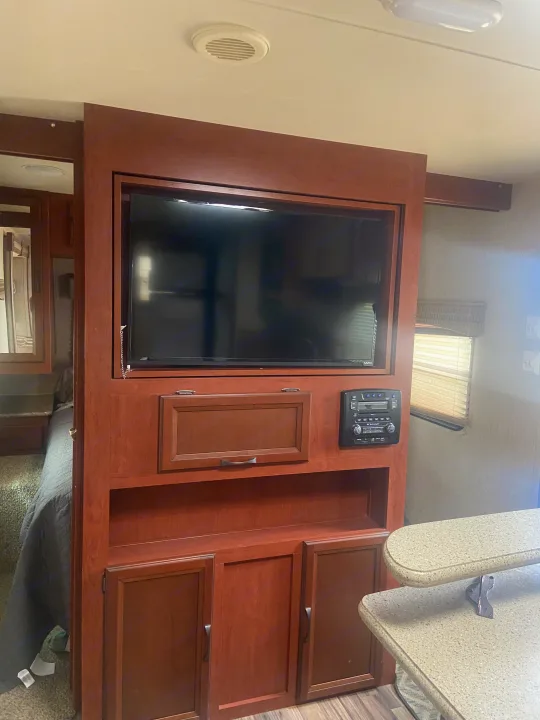 Inside this RV rental: a large wooden entertainment center with TV, stereo, and ample storage, separating the living area from the bedroom.. Palomino Puma 2015