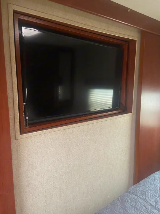 Flat-screen TV, mounted in wood-trimmed alcove, within an RV rental bedroom. Light textured walls & a glimpse of a quilted bed.. Palomino Puma 2015
