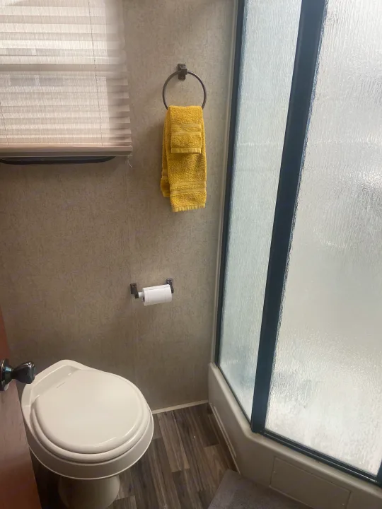 Inside an RV rental bathroom: a white toilet, yellow towels on wall, and textured glass shower enclosure. Space-efficient design.. Palomino Puma 2015