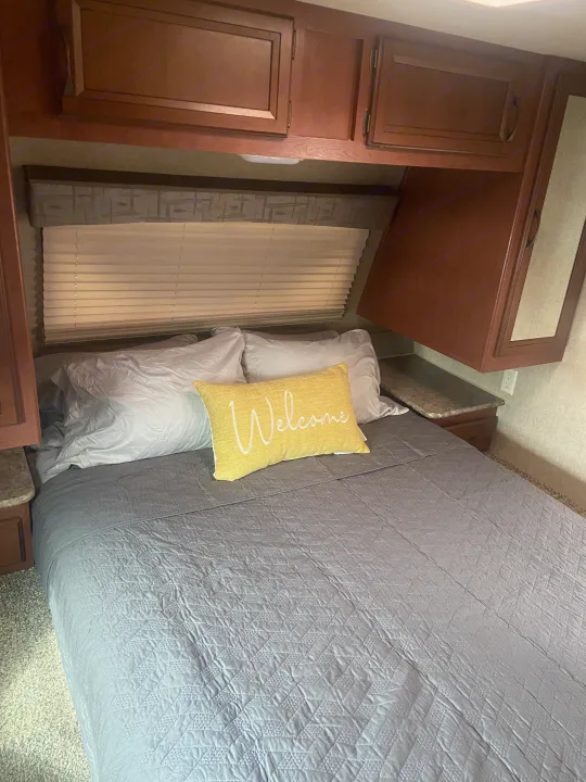 Cozy RV rental bedroom featuring a bed with gray comforter, white pillows, and a yellow 'Welcome' cushion.. Palomino Puma 2015