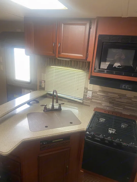 Spacious RV rental kitchen featuring a sink, gas stove, microwave, and overhead cabinets for a comfortable trip.. Palomino Puma 2015