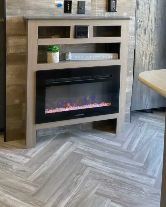 Inside an RV rental: a cozy electric fireplace with colorful flames, display shelves, and stylish gray herringbone floor.. Keystone RV Hideout 2021