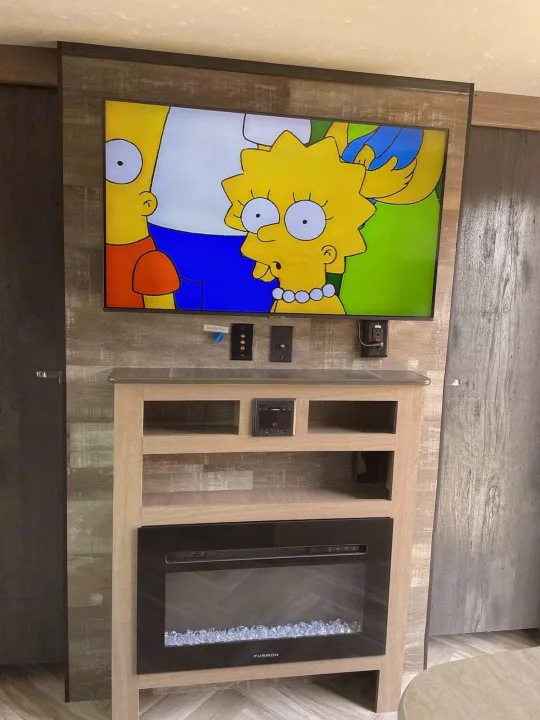 RV rental interior: A TV displays The Simpsons over an electric fireplace and entertainment unit.. Keystone RV Hideout 2021