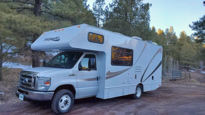 White Class C Majestic RV rental parked on a dirt road, surrounded by pine trees with some snow on the ground.. Thor Majestic 2014