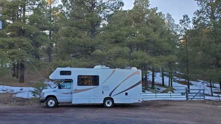 White Class C RV rental parked on a dirt road against a snowy pine forest backdrop. Ready for adventure and a scenic road trip.. Thor Majestic 2014