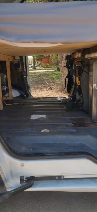View from inside an RV rental looking out the back. The van's interior shows a basic floor, wooden frame, and exposed seat mechanism.. Ford Transit Custom 2011