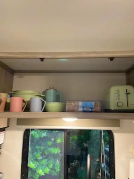 Organized RV rental kitchen shelves display mugs, bowls, a teapot, and a toaster, perfect for travel cooking needs.. Keystone RV Passport SL 2021