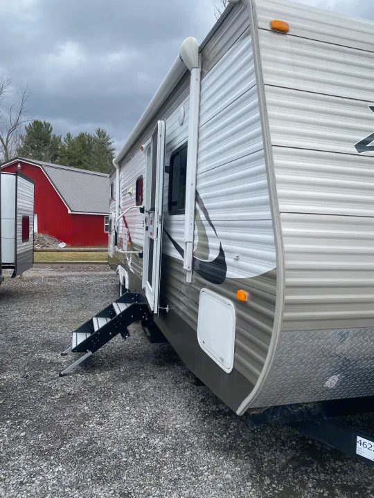 A modern RV rental with an open door and steps, parked on gravel. A red barn is visible in the background.. Crossroads RV Zinger 2015