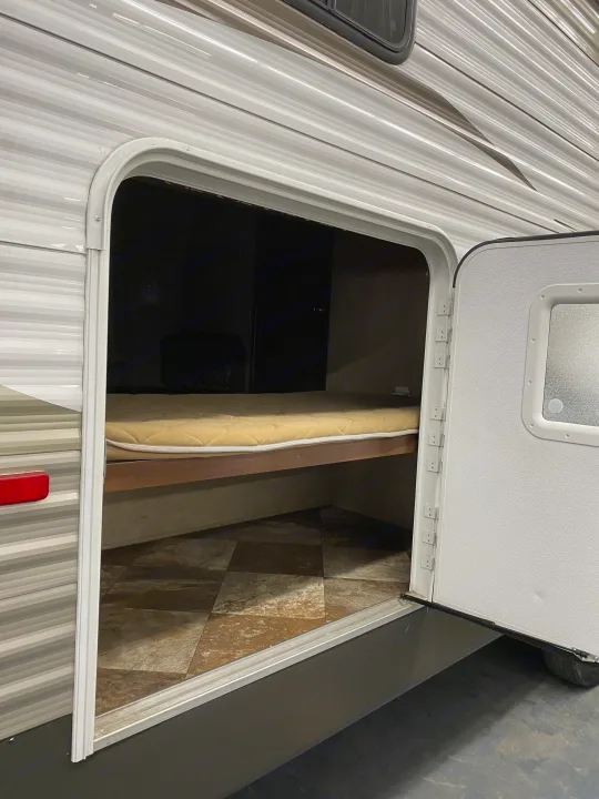 A practical rv rental feature: open side door shows a bunk bed with mattress and tiled floor, suitable for sleeping or storage.. Crossroads RV Zinger 2015
