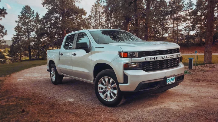 This silver Chevrolet Silverado pickup is parked on a dirt road, surrounded by tall pine trees, ideal for an RV rental adventure.. Chevrolet Silverado 2021