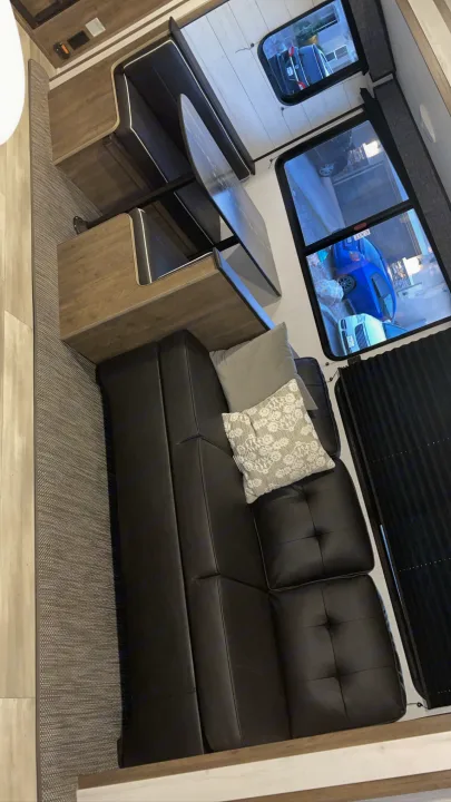 RV rental interior: cozy black leather sofa, wood dinette, and large windows revealing cars outside, showing the spacious layout.. Heartland Pioneer 2022