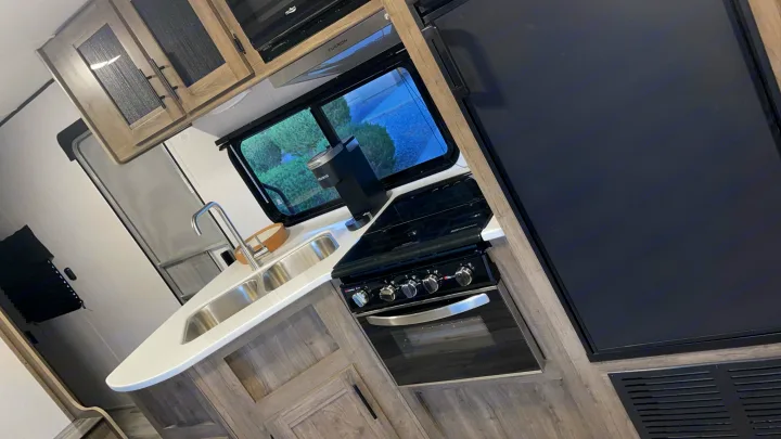 RV rental kitchen featuring a modern stove, sink, coffee maker, and refrigerator, all set for your next adventure.. Heartland Pioneer 2022