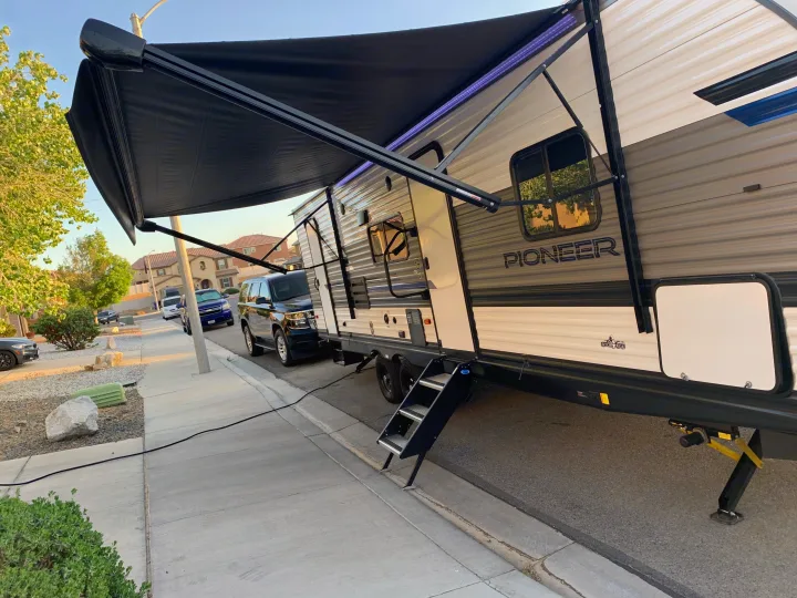Extended awning with purple LED lights on a 'Pioneer' RV rental, parked street-side with entry steps down.. Heartland Pioneer 2022