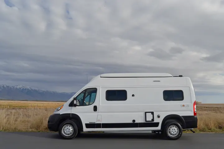 White Winnebago Solis RV rental parked by snowy mountains & fields under cloudy sky. Perfect for adventure!. Winnebago Solis 2021