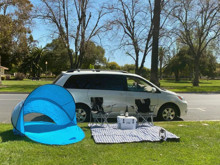 Park picnic setup with tent, chairs, & cooler by a minivan. Enjoy similar freedom on your next RV rental trip.. Custom Camper 2004