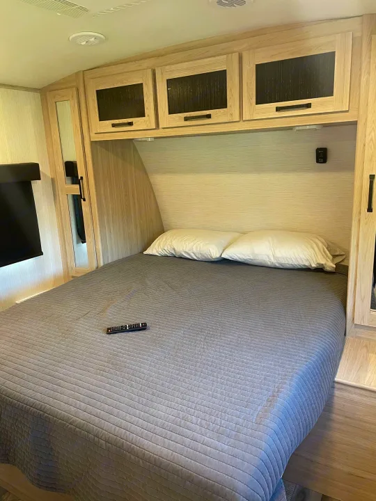 Experience comfort in this RV rental bedroom, featuring a full bed with gray bedding, sleek wood cabinets, and modern amenities.. Heartland Sundance 294BH 2022
