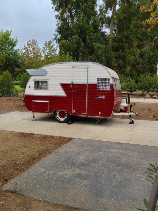 Retro red & white Shasta travel trailer, parked at a campsite, ready for your next RV rental adventure.. Shasta 1500 1956