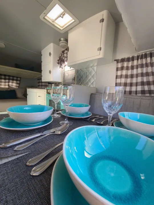 Charming RV rental interior: set dining table, kitchenette with aqua accents, and cozy bunk beds. Perfect for glamping!. Shasta 1500 1956