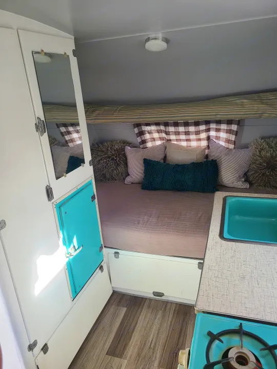 RV rental: Cozy camper interior, featuring a bed with pillows, teal sink, and stove setup.. Shasta 1500 1956