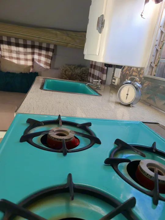 Inside an RV rental: a compact kitchen with vintage teal stovetop, matching sink, and patterned counter. Ready for adventure!. Shasta 1500 1956