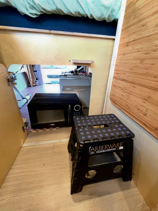 RV rental interior: Microwave & foldable step stool inside a compact camper setup with light wood walls.. Mercedes-benz Sprinter 2016