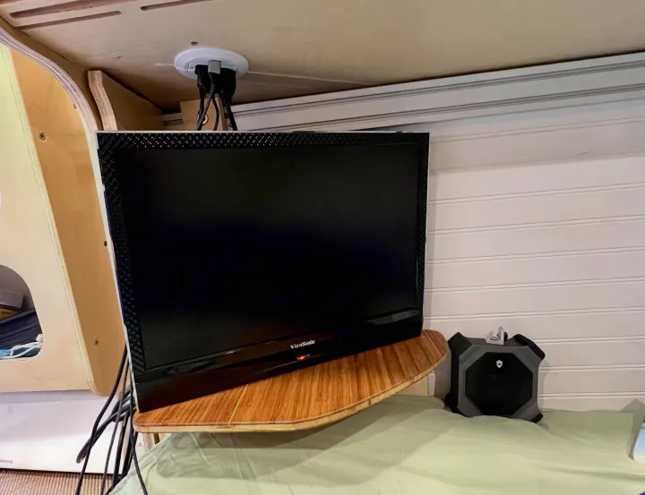 An RV rental's cozy entertainment corner: ViewSonic TV on a wood shelf, cables discreetly routed, beside an Alienware speaker on light green bedding.. Mercedes-benz Sprinter 2016