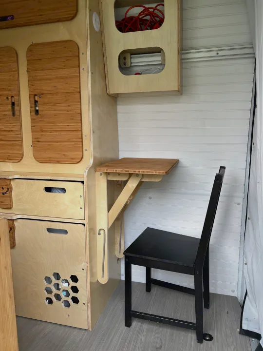 Inside this RV rental: custom wood storage, drawers, and a bamboo fold-down table with a chair, designed for compact living.. Mercedes-benz Sprinter 2016