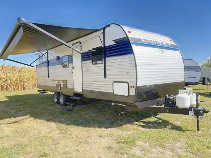 Brightly lit Prime Time Avenger LE travel trailer with extended awning, ideal for rv rental camping. Note propane tanks.. Prime Time Avenger 26DBSLE 2022