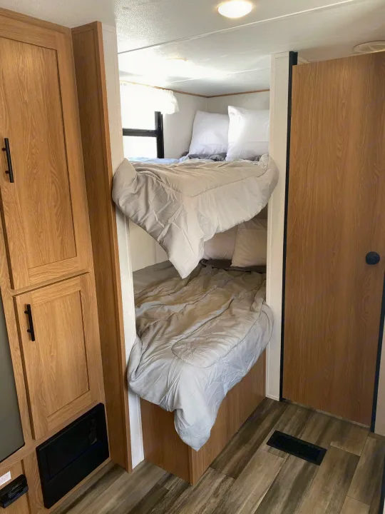 RV rental interior showcasing comfortable bunk beds, light bedding, and warm wood cabinetry, ideal for family trips.. Prime Time Avenger 26DBSLE 2022