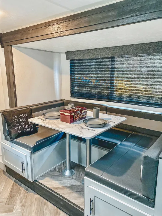 Inside an RV rental: a cozy camper dinette with a marble table, plates, S'mores kit, and a fun pillow about parking.. Forest River Other 2022
