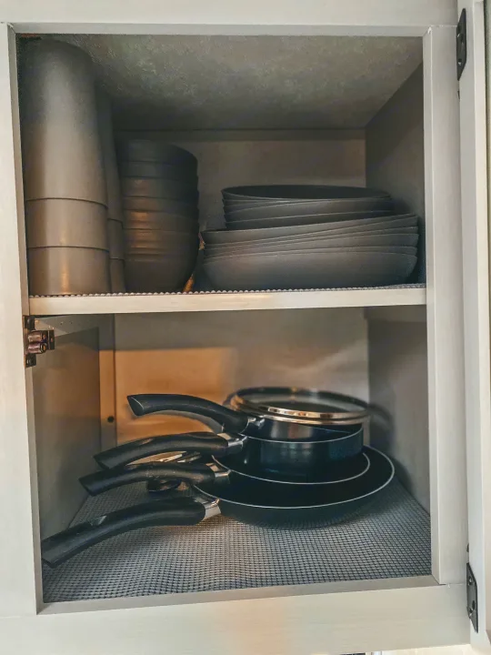 RV rental kitchen storage: neatly stacked grey bowls/plates & black frying pans on lined shelves within a light-colored cabinet.. Forest River Other 2022