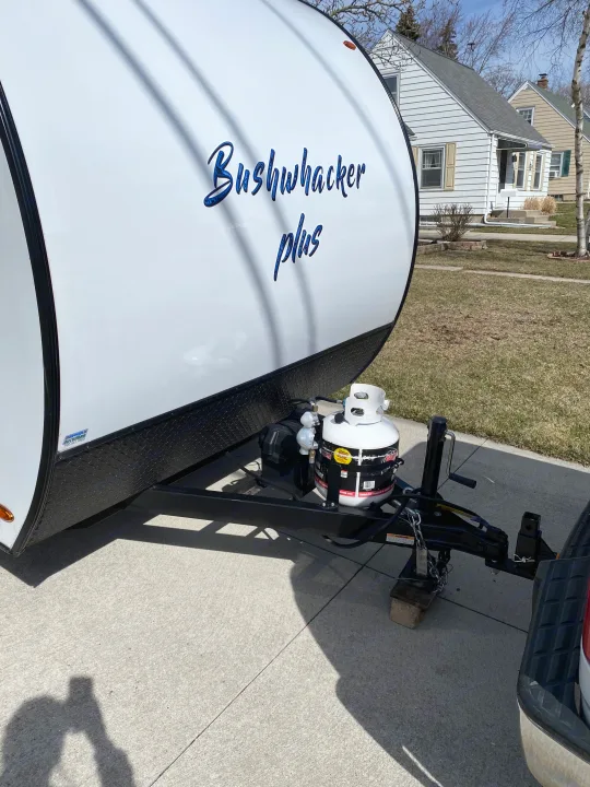 Bushwhacker Plus travel trailer (RV rental) parked on a driveway. Front hitch and propane tank visible for adventures.. Braxton Creek Bushwhacker Plus 2022