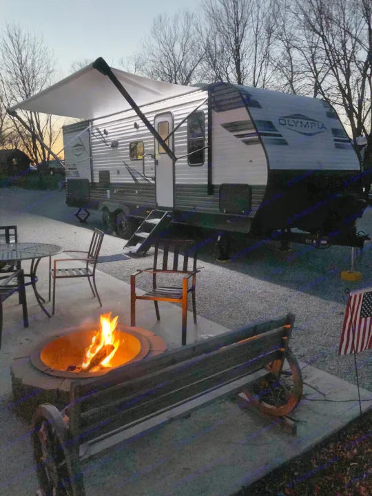 Enjoying an RV rental at dusk: a bright campfire glows next to a large travel trailer with awning & lights.. Highland Ridge Olympia 26BHS 2022