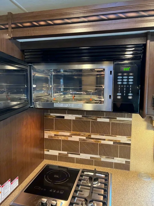 RV rental kitchen featuring a modern, open microwave/convection oven above a multi-burner stovetop and tiled backsplash.. Thor Motor Coach Four Winds 2018