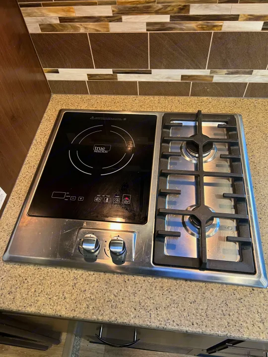 RV rental kitchen: a sleek hybrid cooktop featuring a True Induction electric burner and a two-burner gas stove.. Thor Motor Coach Four Winds 2018