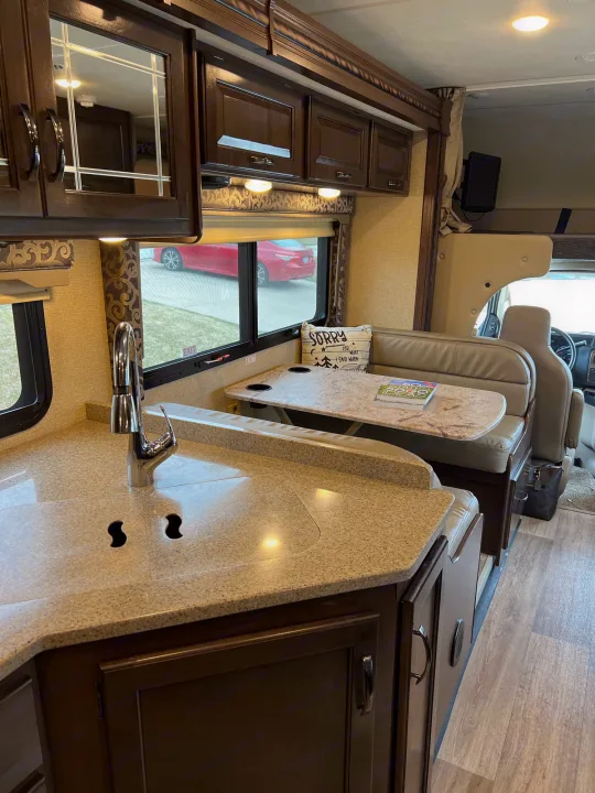 Well-lit rv rental interior with a light-colored kitchen countertop, chrome sink, and adjacent dinette seating.. Thor Motor Coach Four Winds 2018
