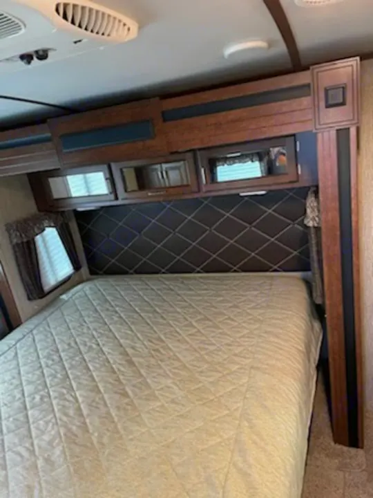 RV rental bedroom interior with a comfy bed, overhead cabinets, and a diamond-patterned headboard.. Keystone Outback 2018