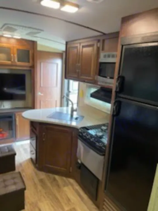 Inside a modern RV rental: kitchen with fridge, stove, sink, and living area with TV & fireplace for your trip.. Keystone Outback 2018
