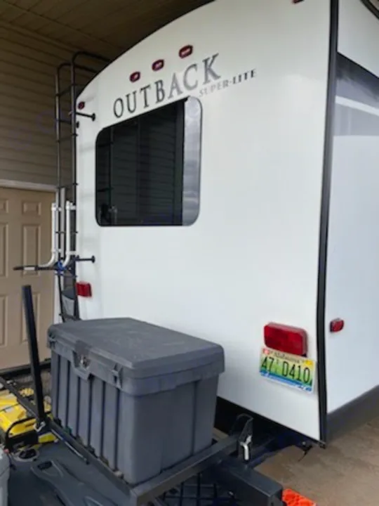 Rear view of an Outback Super-Lite RV rental, with a ladder on the left and a cargo carrier holding a storage box at the bottom.. Keystone Outback 2018