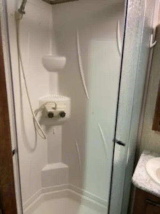 This compact, white RV rental shower stall features an adjustable shower head, built-in shelves, and a clear glass door—perfect for road trips.. Keystone Outback 2018
