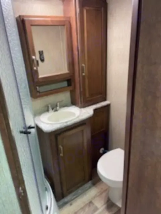 This RV rental bathroom features a dark wood vanity, sink, mirror, toilet, and shower stall. Clean, compact, and functional.. Keystone Outback 2018