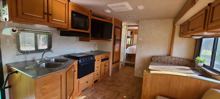 Spacious RV rental interior featuring a full kitchen with sink, stove, microwave, and fridge, plus dining area and bedroom view.. Jamboree Jamboree Motorhome 2011