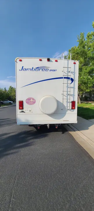 White "Jamboree Sport" RV rental with spare tire and ladder, parked on asphalt.. Jamboree Jamboree Motorhome 2011